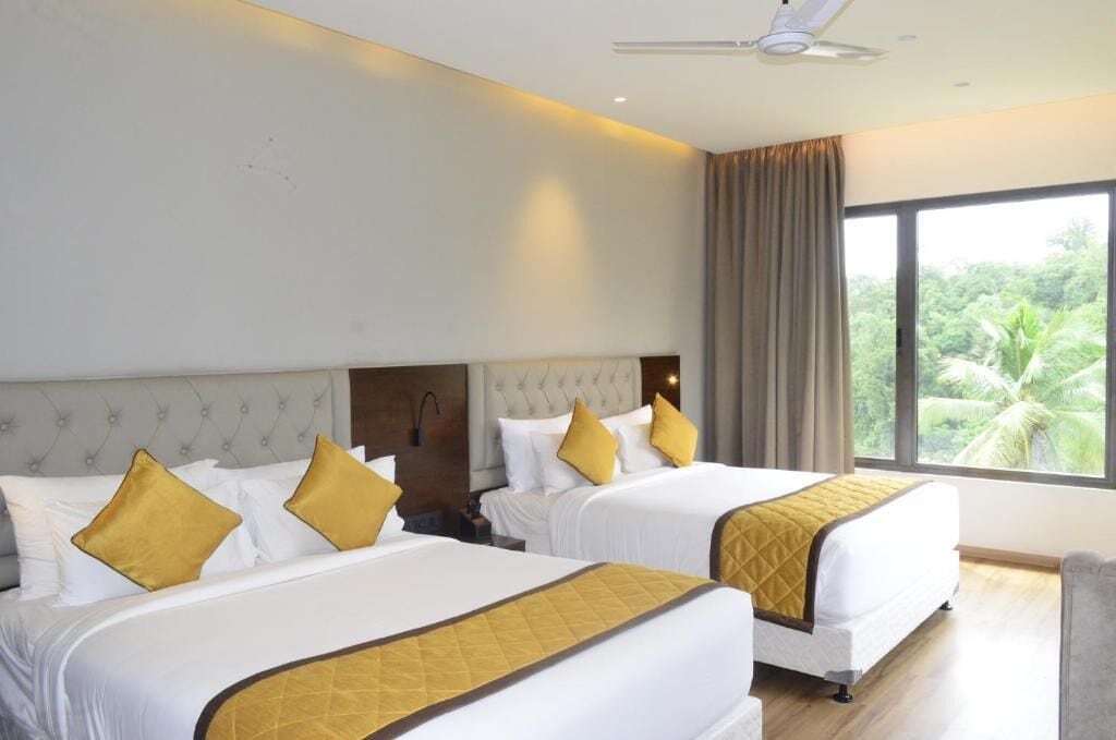 Hotelkamer met twee bedden, een plafondventilator en een groot raam met uitzicht op groen.
