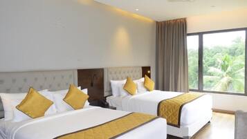 Hotelkamer met twee bedden, een plafondventilator en een groot raam met uitzicht op groen.
