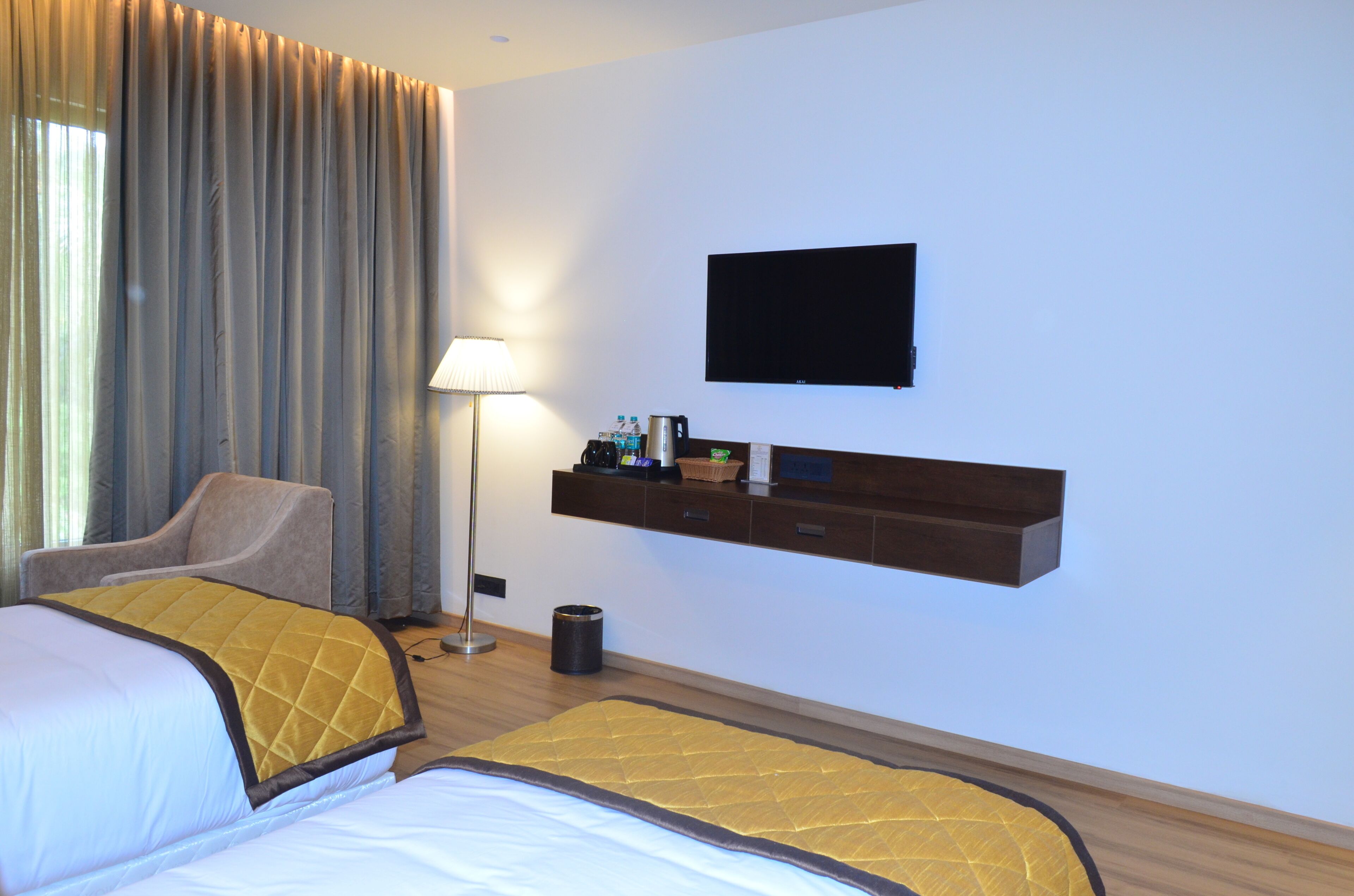 A hotel room with a bed, a chair, a TV mounted on the wall, and a shelf with items.