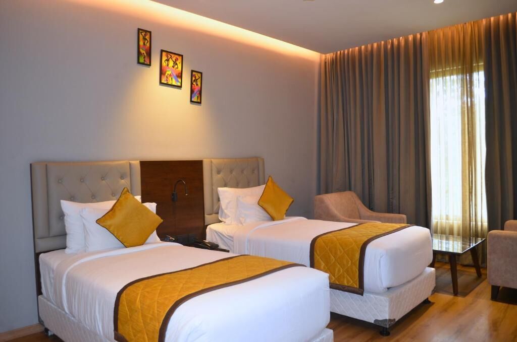 A hotel room with two beds, a sofa, a table, and a window with curtains.