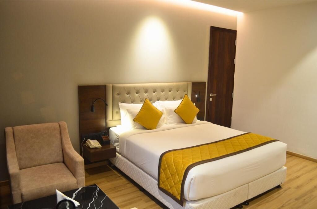 A hotel room with a bed, a chair, a nightstand, and a door.