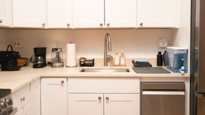 Een moderne keuken met witte kastjes, een roestvrijstalen spoelbak, een koffiezetapparaat en een waterdispenser.