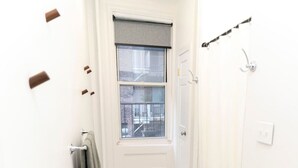 Een badkamer met een raam, een handdoekhouder, een douchegordijnstang en een marmeren vloer.