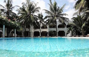 Una piscina con palmeras y un edificio de ventanas arqueadas.