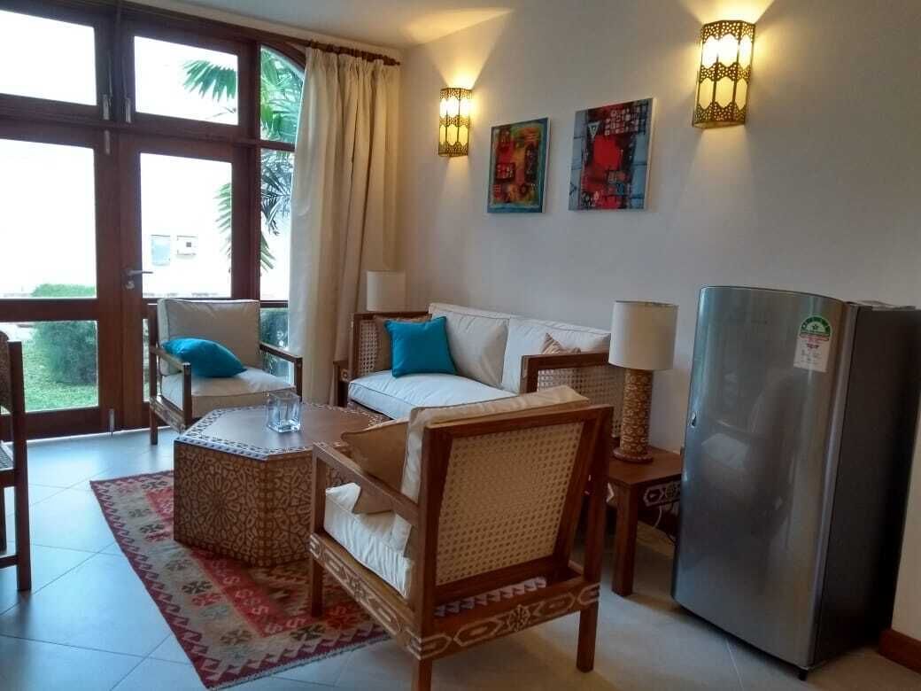 Ein Zimmer mit einer Couch, einem Esstisch, einem Kühlschrank und einem Fenster mit Vorhängen.