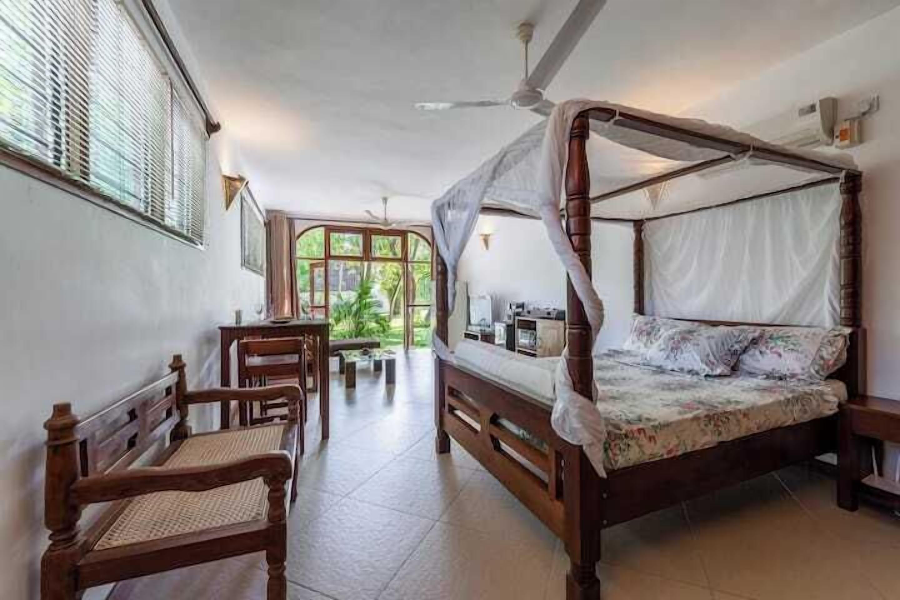 Una habitación con una cama con dosel, un escritorio con una silla y una ventana con persianas.