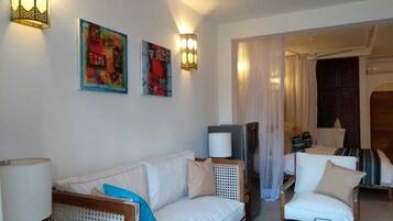A living room with a sofa, armchairs, a coffee table, a television, and wall-mounted lamps.