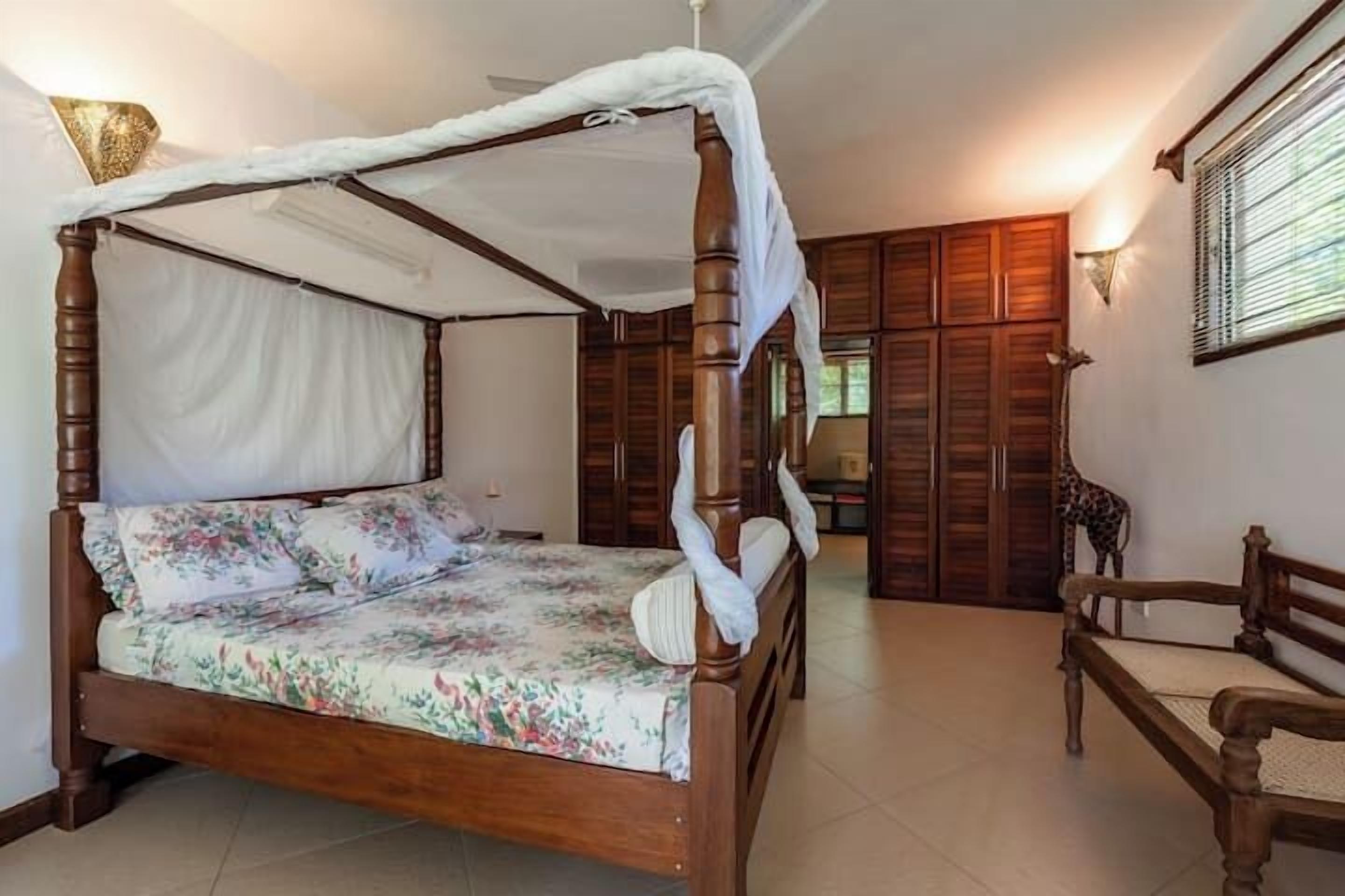 A four-poster bed with a canopy, a wooden chair, and a giraffe statue.