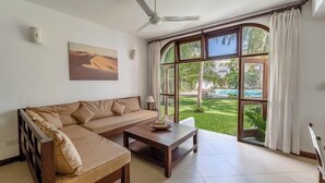 A modern living room with a sofa, a coffee table, and a large window with a view of a pool and greenery.