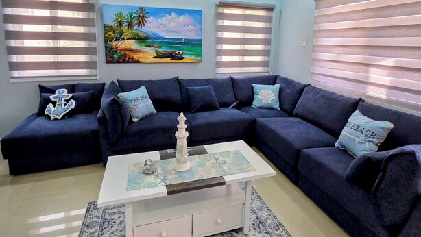 Ein Wohnzimmer mit Ecksofa, Couchtisch, Deckenventilator und einem Strandbild.