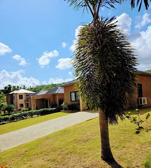 A modern building with a paved walkway, a palm tree, and a clear blue sky. - 2-bedroom bungalow in beautiful Ocho Rios gated community  with AC. (Ocho Rios)