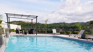 Ein klares Schwimmbecken mit Liegestühlen und einer Pergola, umgeben von Grünflächen und Hügeln.