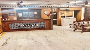 A reception desk with a 'RECEPTION' sign, wooden cabinets, a potted plant, a clock, and a sofa. - Hotel Le Mount (New Delhi)