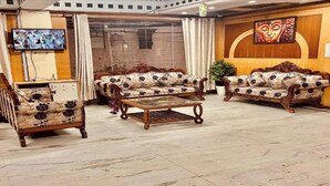 A lobby with two sofas, a coffee table, a television, and a wall with a painting. - Hotel Le Mount (New Delhi)