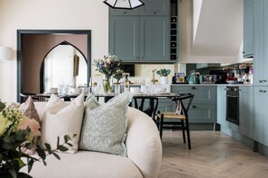 Eine moderne Küche mit türkisfarbenen Schränken, ein Essbereich mit weißem Tisch und Stühlen sowie eine gemütliche Sitzecke mit einer Couch und Kissen.