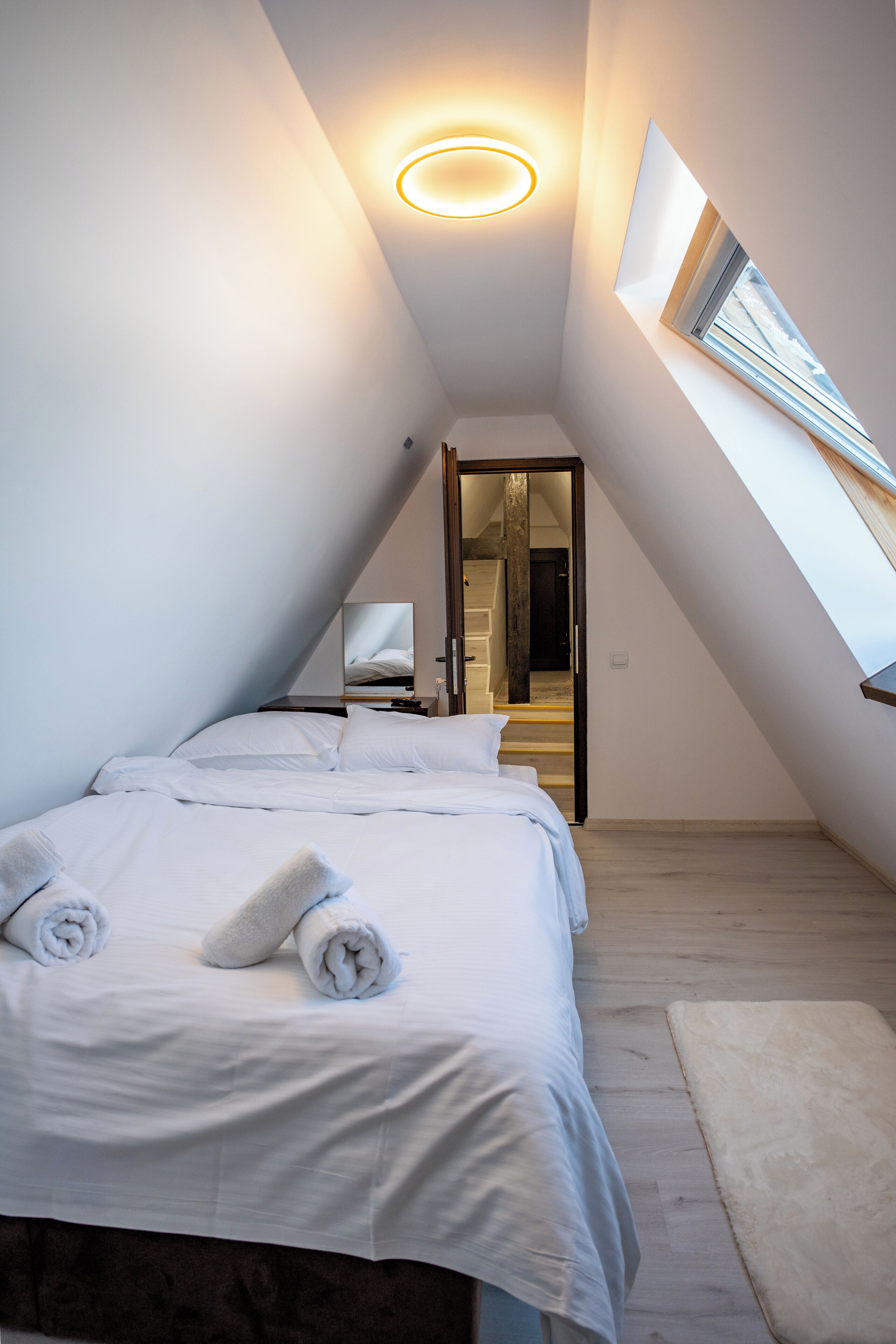 A modern bedroom with a skylight, a bed with white linens, and a wooden floor.