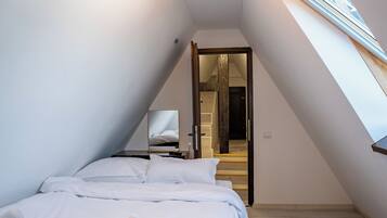 A modern bedroom with a skylight, a bed with white linens, and a wooden floor.