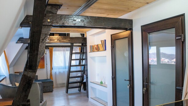 A loft-style room with a wooden ceiling, a desk, a chair, a ladder, and a door with a view. - Barrique Milescu 5 (Brașov)