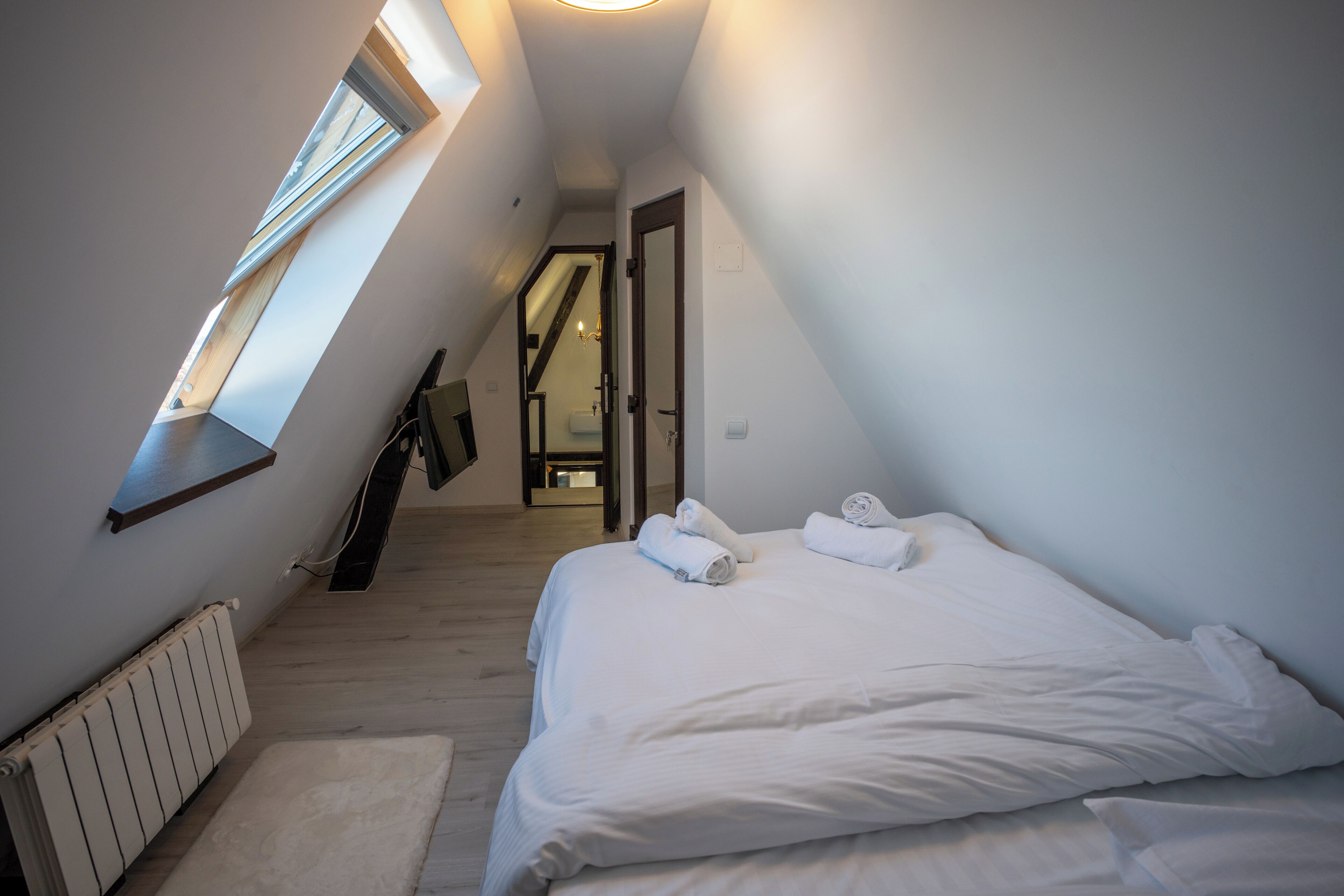 A bedroom with a sloped ceiling, a skylight, a bed with white linens, and a radiator.