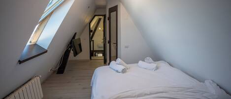 A bedroom with a sloped ceiling, a skylight, a bed with white linens, and a radiator.