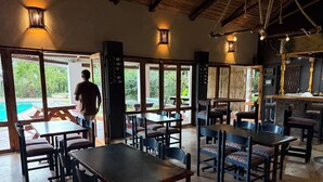 An indoor dining area with tables and chairs, a bar area, and large windows offering views of the outdoors.