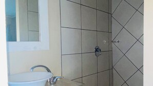 A bathroom with a sink, mirror, and shower area.