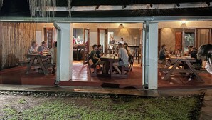 An outdoor dining area with multiple tables and chairs, a covered walkway, and a building with a corrugated metal roof.