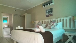 A bedroom with a bed, a bedside table, a nightstand, a window, and an air conditioning unit.