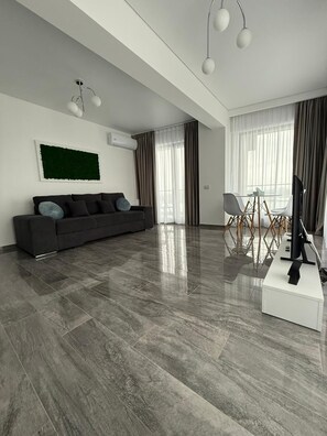Ein modernes Wohnzimmer mit einem dunkelgrauen Sofa, einem weißen Couchtisch und einem Flachbildfernseher auf einem weißen Schrank.