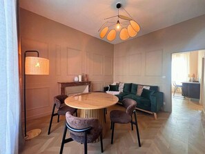 Ein modernes Wohnzimmer mit einem runden Holztisch, vier Stühlen, einem grünen Sofa, einer Stehlampe und einer außergewöhnlichen Deckenleuchte.