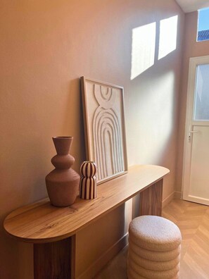 Ein Flur mit einem hölzernen Konsolentisch, einem gerahmten Kunstwerk, einer Vase und einer gestreiften Vase.