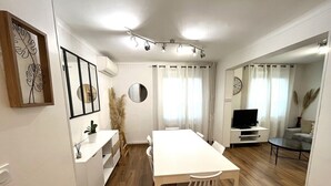 Un soggiorno moderno con un tavolo da pranzo in legno, divani bianchi, una TV e un'ampia finestra con tende.