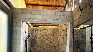 Un baño con pared de piedra, ducha y lavamanos.