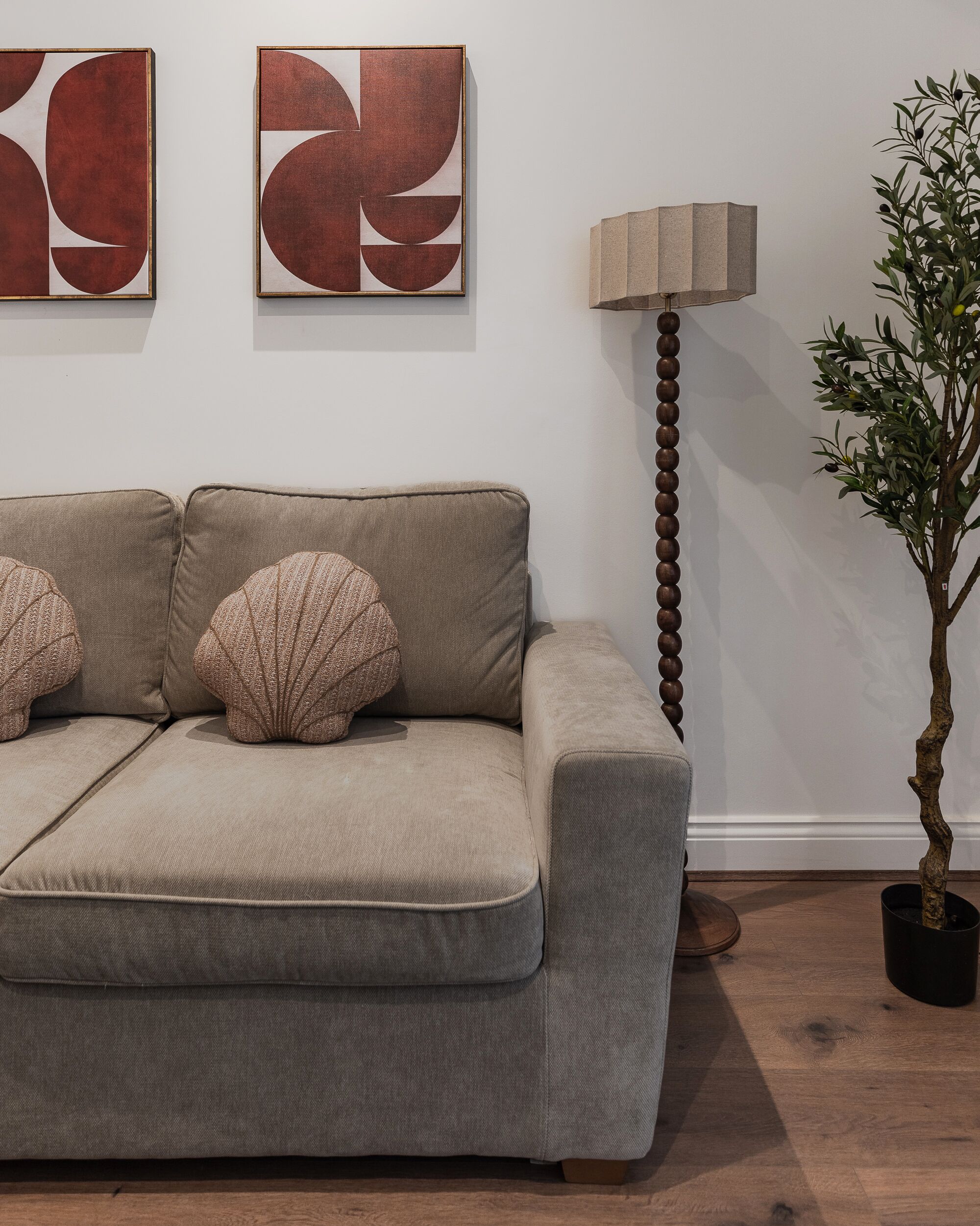 A beige sofa with patterned cushions, a floor lamp, and a potted plant in a room with a wooden floor.