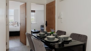 Un comedor moderno con una mesa negra, sillas grises y vistas a un dormitorio con una cama y una ventana.