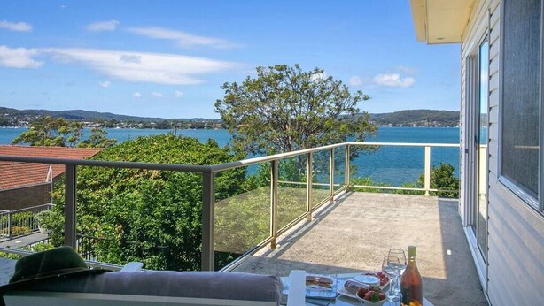 Un balcon avec vue sur la mer, une table garnie de nourriture et de boissons, et un arbre.