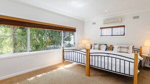 Une chambre à coucher avec un lit, une fenêtre avec des stores, un appareil de climatisation et une petite table avec une lampe.