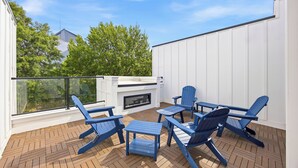Eine Dachterrasse mit Kamin, Sitzgelegenheiten im Freien und Blick auf Bäume und Gebäude.