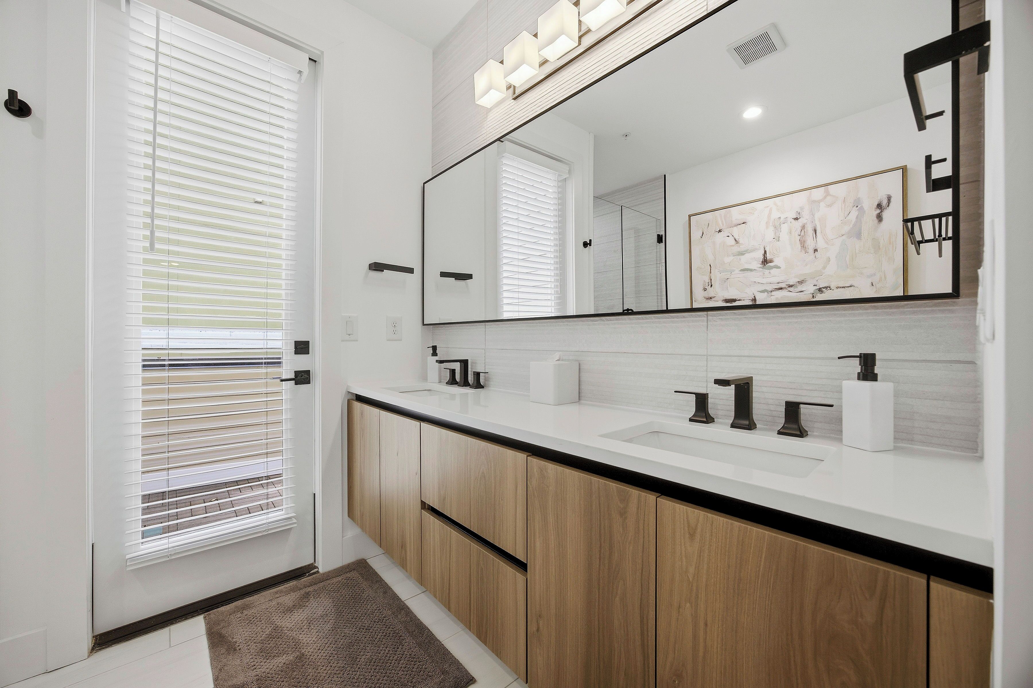 A modern bathroom with a large mirror, two sinks, wooden cabinets, and a towel rack.