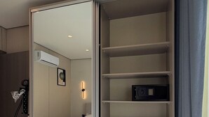 Habitación de hotel con cama, armario con estantes múltiples, mesita de noche y aire acondicionado de pared.