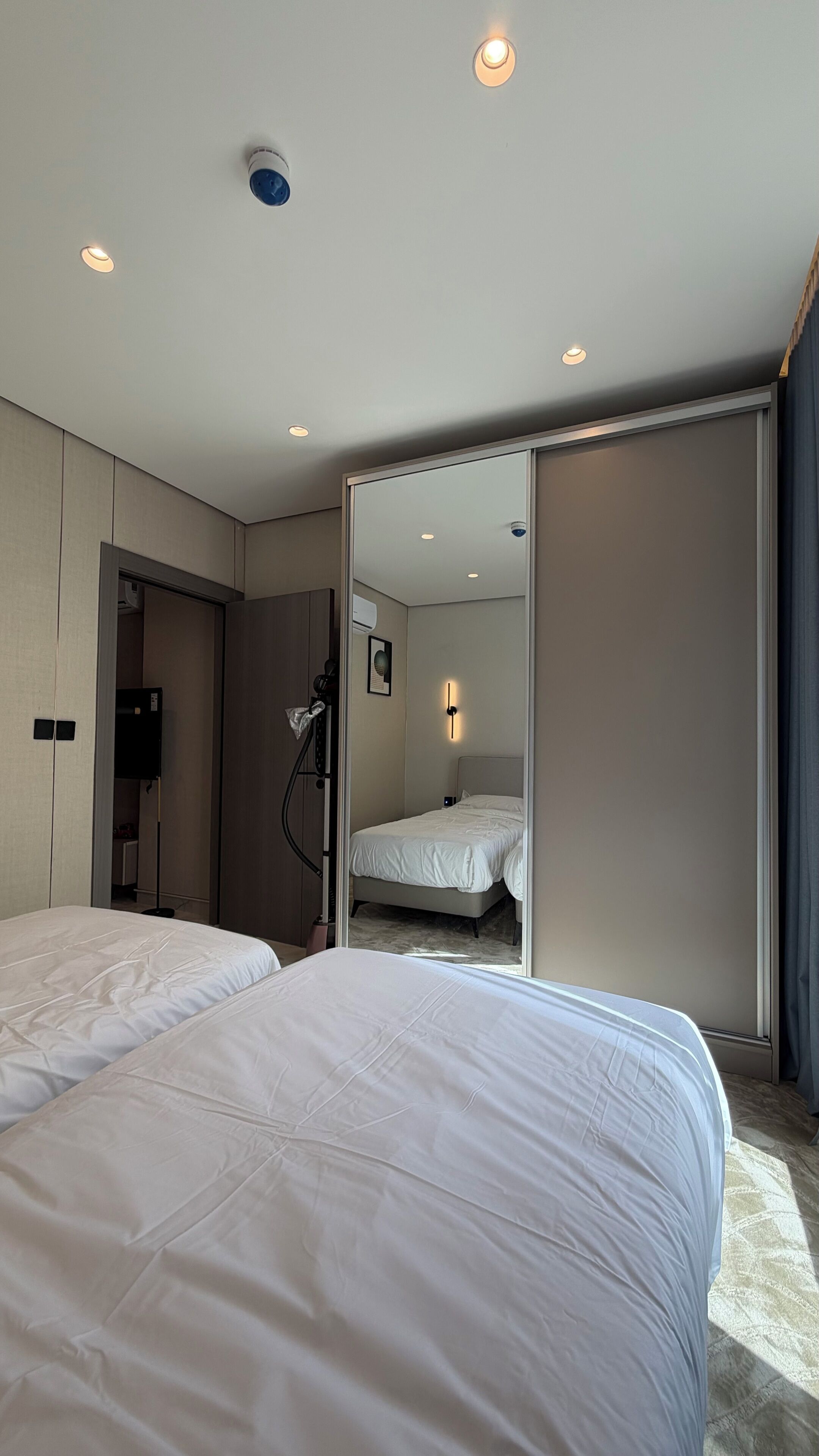 A hotel room with two beds, a sliding door, a ceiling light, and a wall-mounted air conditioning unit.