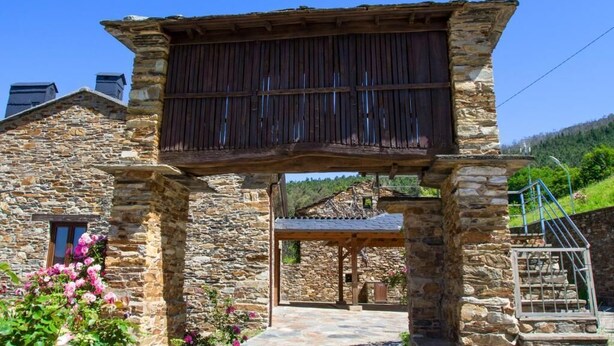 A stone building with a wooden pergola entrance, a stone staircase, and a view of the surrounding landscape.