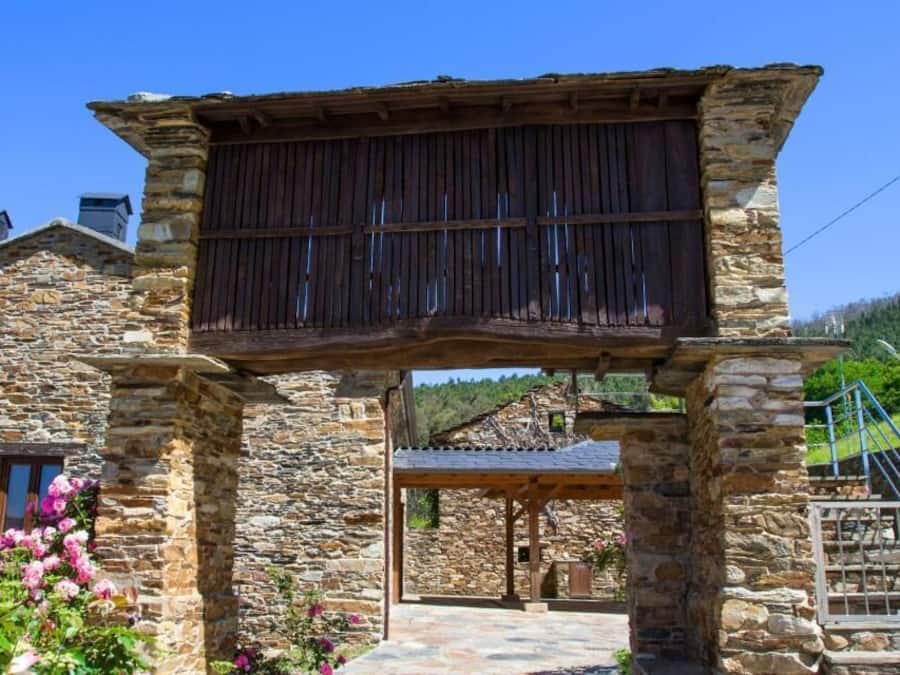 A stone building with a wooden pergola entrance, a stone staircase, and a view of the surrounding landscape.