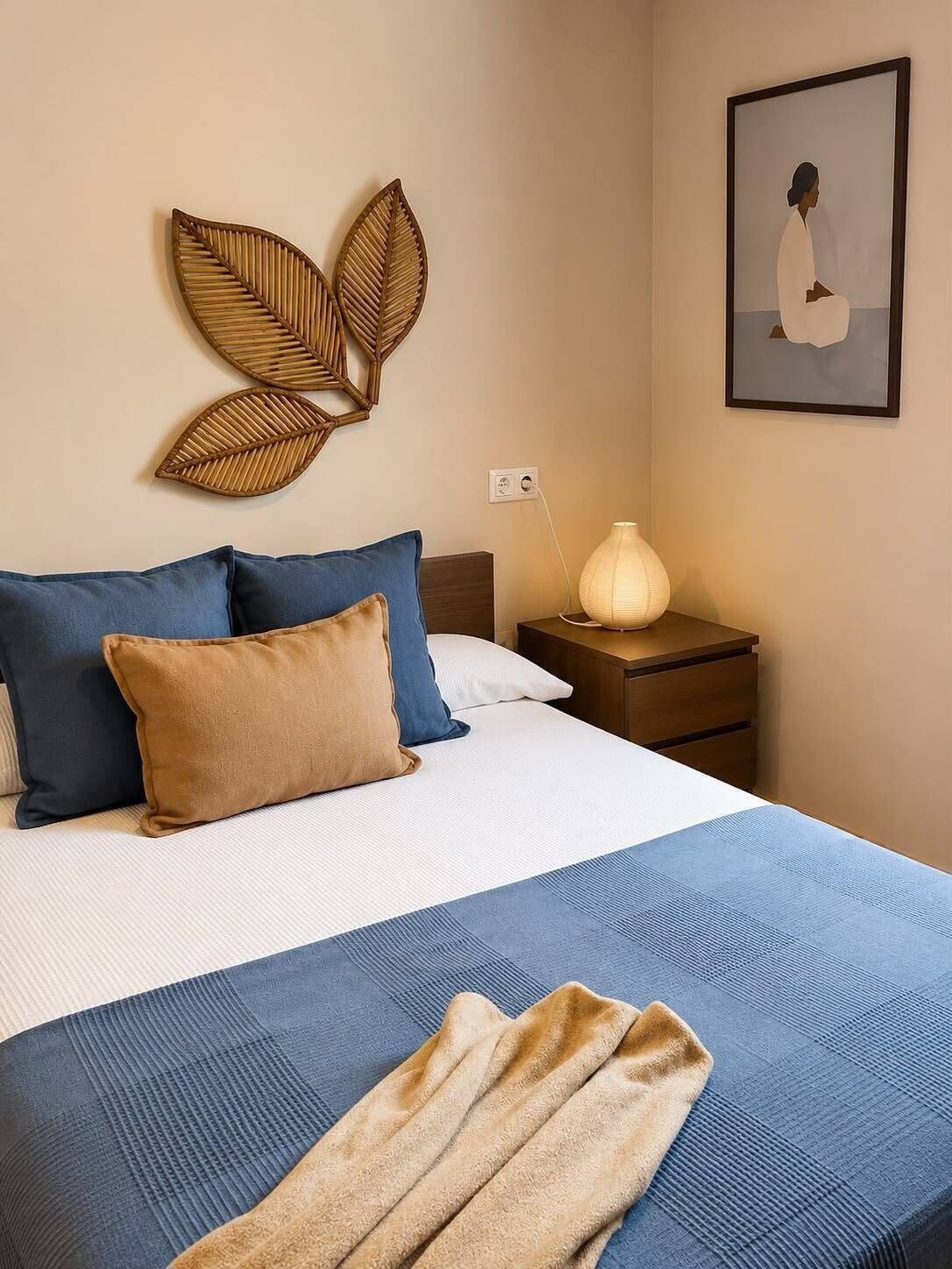 A neatly made bed with a blue and white bedspread, a brown throw blanket, and two pillows.