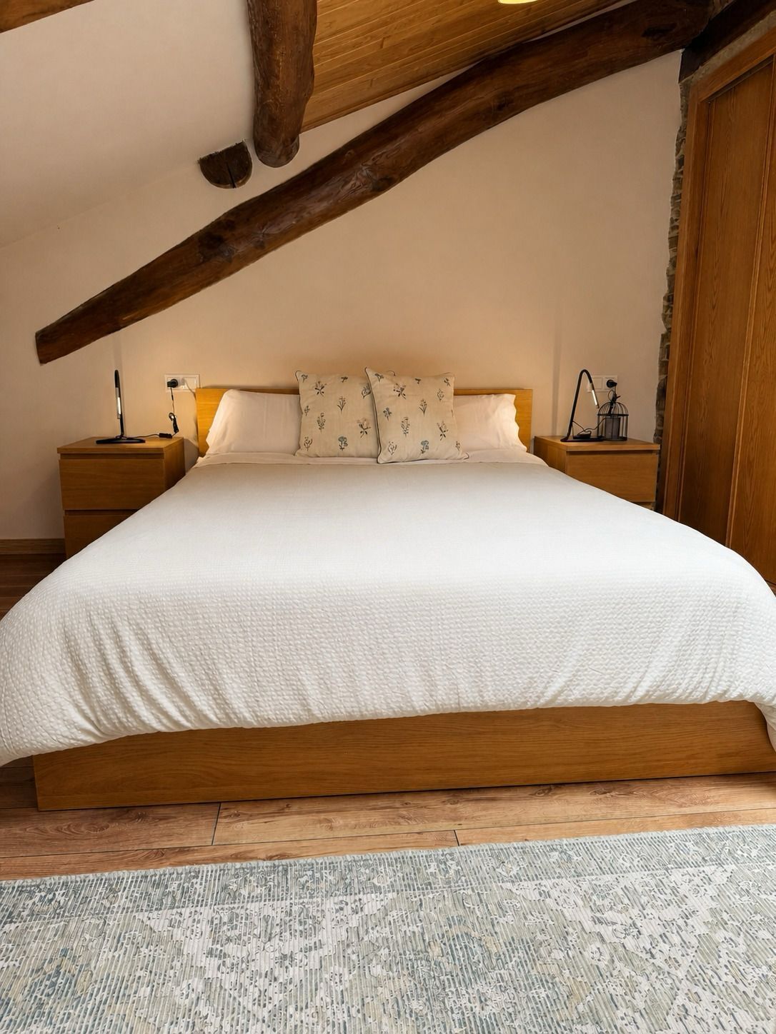 Een slaapkamer met een groot bed, een houten hoofdbord, twee nachtkastjes met lampen en een kamerkleed met dessin.