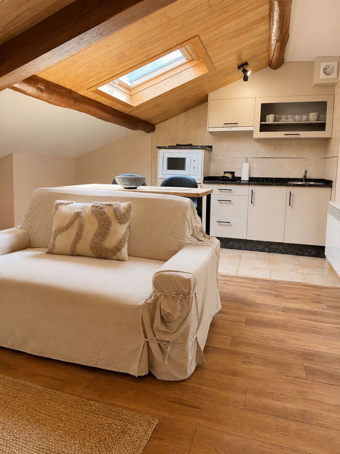 Una habitación acogedora con sofá cubierto, zona de cocina y tragaluz.