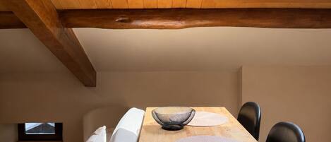A cozy room with a wooden ceiling, a skylight, a wooden dining table with chairs, and a bed with pillows.