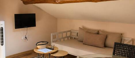 Una habitación acogedora con techo inclinado, un sofá, una mesa de vidrio y un televisor montado en la pared.