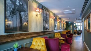 A restaurant with a long counter, cushioned chairs, and framed artwork on the walls. - Black Cap Camden (London)