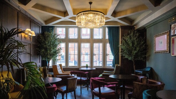 A room with a large window, multiple chairs, tables, and a chandelier. - Black Cap Camden (London)
